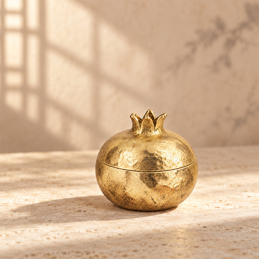 Gold-toned pomegranate decorative box with its lid closed on a stone surface.
