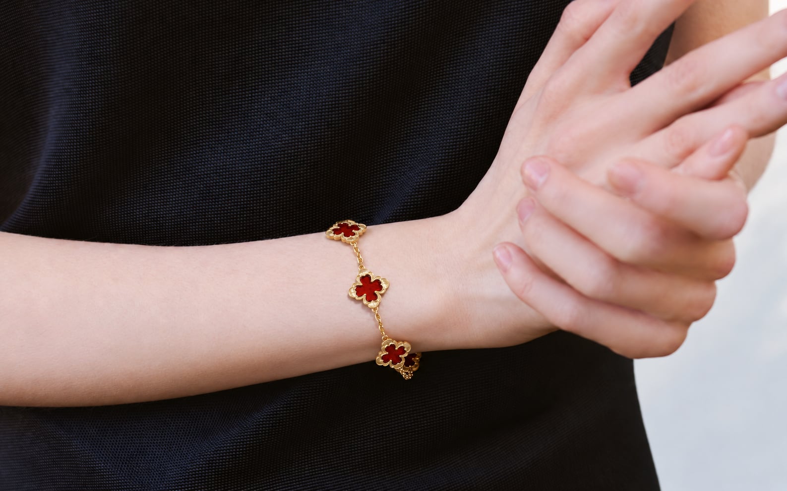 Red flower-motif bracelet with gold-tone links worn on a wrist against a black top