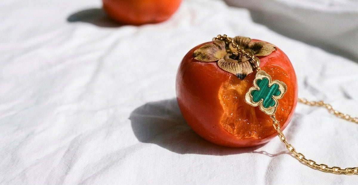 Green clover-shaped pendant and gold-tone chain resting on a persimmon on white fabric