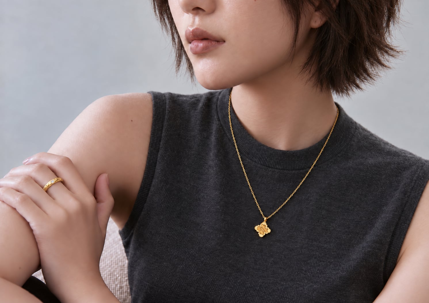 Gold-tone flower pendant necklace worn over a charcoal sleeveless top